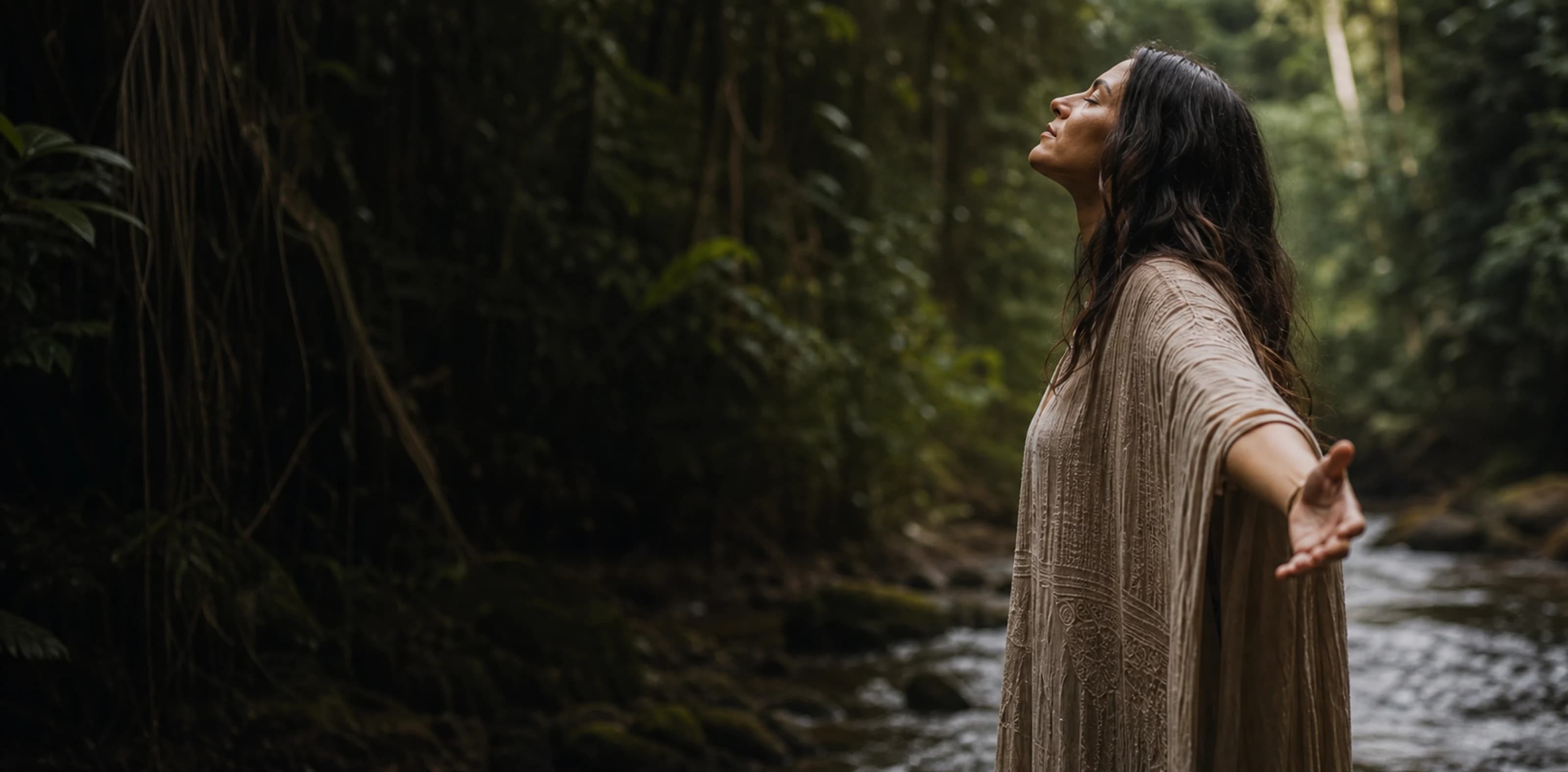 Mulher em contemplação com braços abertos em um riacho dentro da floresta.