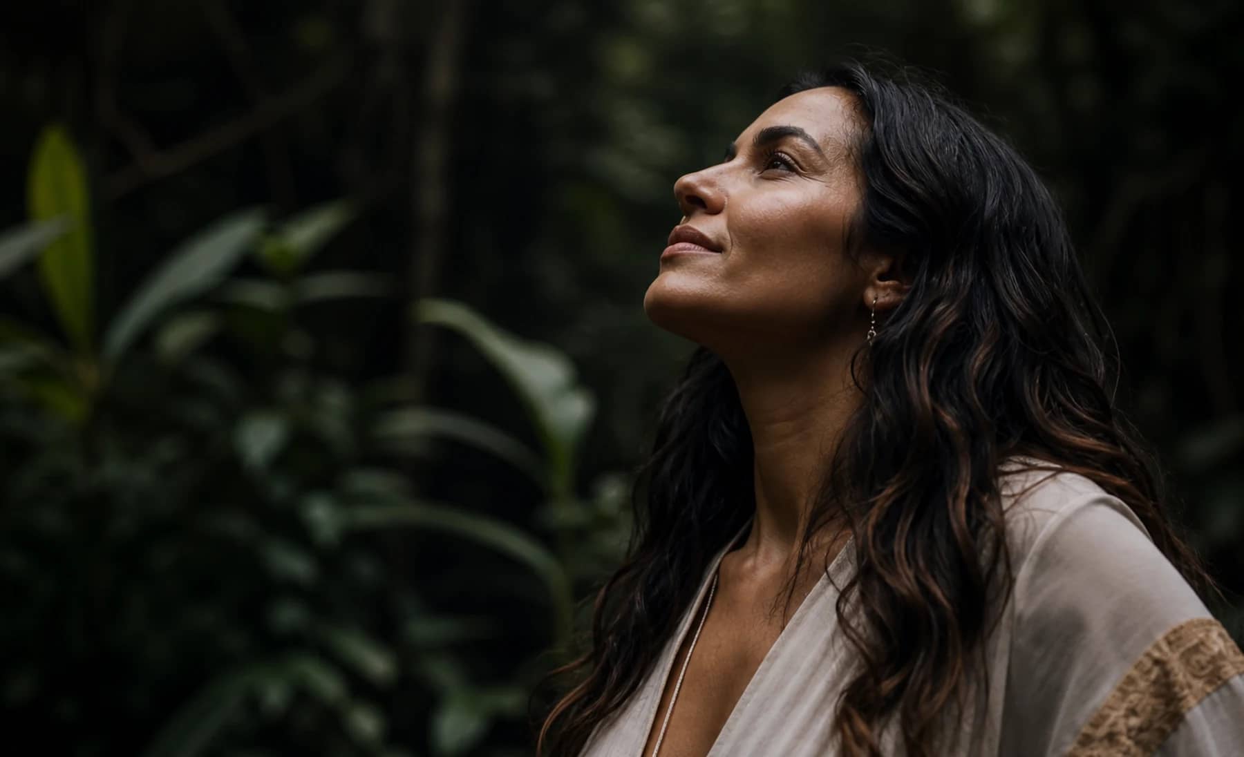 Mulher em floresta olhando serenamente para cima.